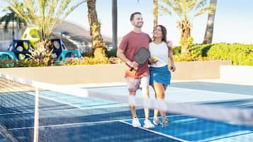 Una cancha de tenis con red, palmeras y un cielo despejado.