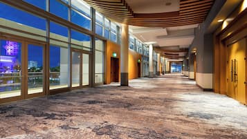A hotel corridor with large windows, a patterned carpet, and wooden ceiling panels.