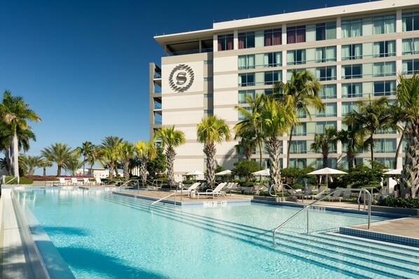 A hotel with a swimming pool, palm trees, and lounge chairs.