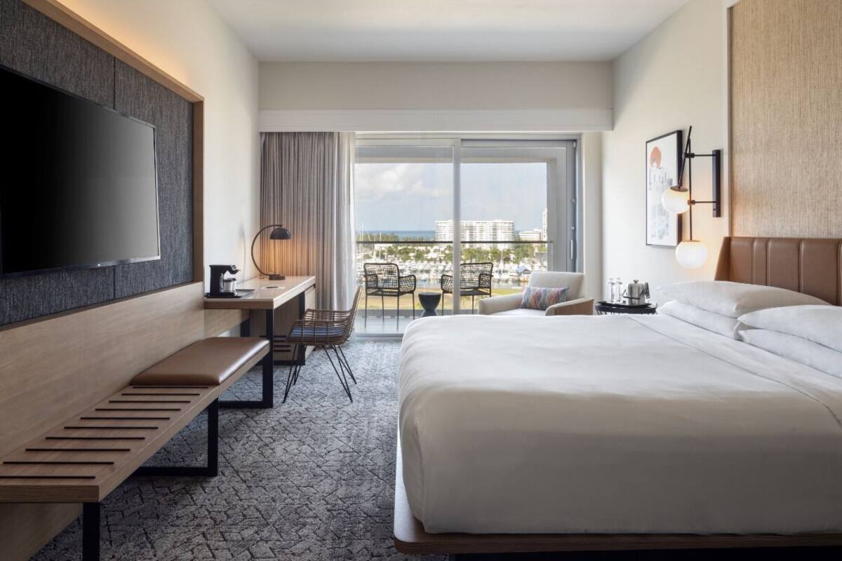 Une chambre d’hôtel avec un grand lit, un bureau avec une chaise, une télévision et un balcon offrant une vue sur la ville.
