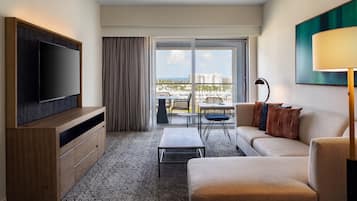 Een moderne hotelkamer met een flatscreen televisie, een bank, een salontafel en uitzicht op de stad door grote ramen.