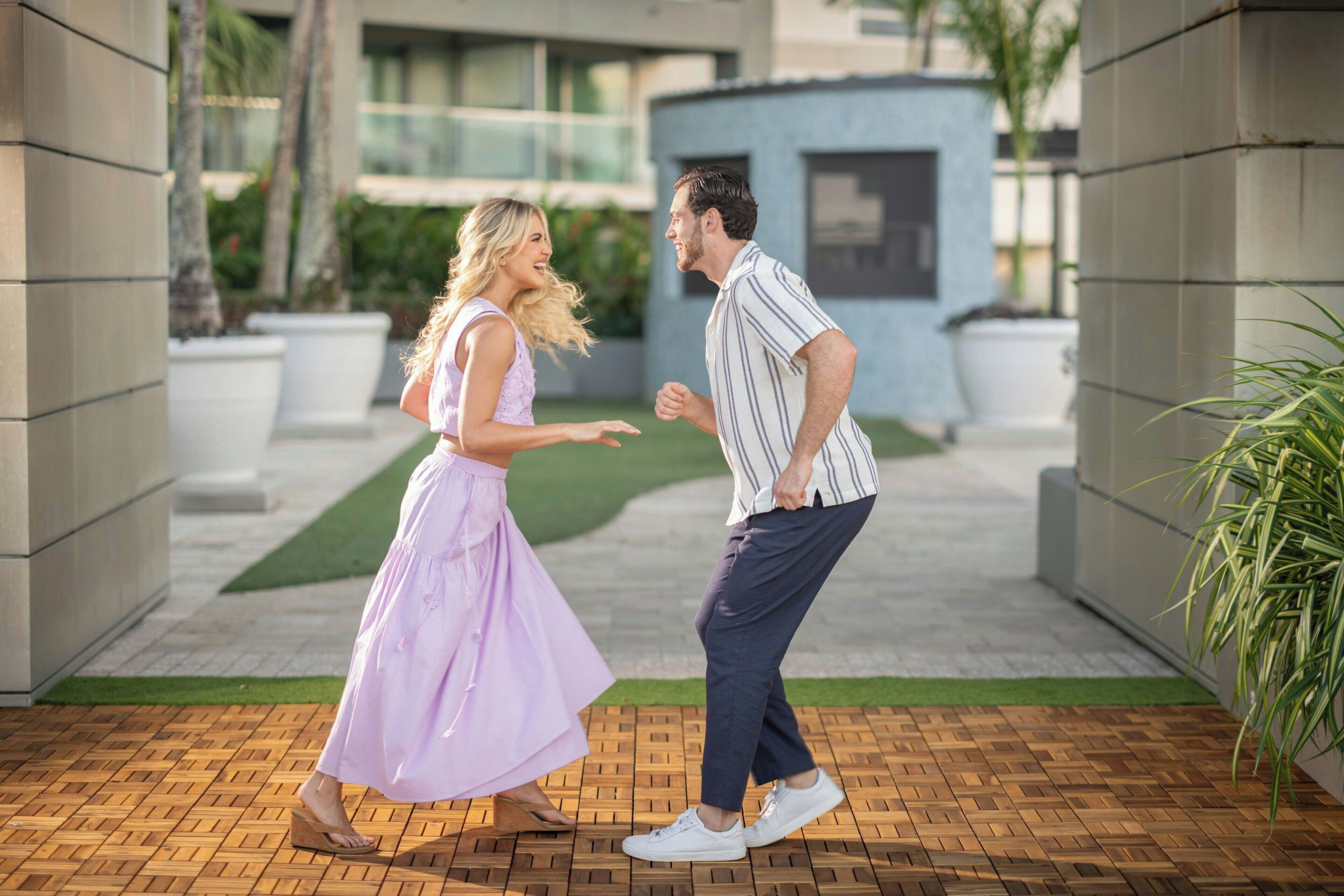 Una pareja bailando en un espacio exterior pavimentado, con un edificio moderno al fondo.