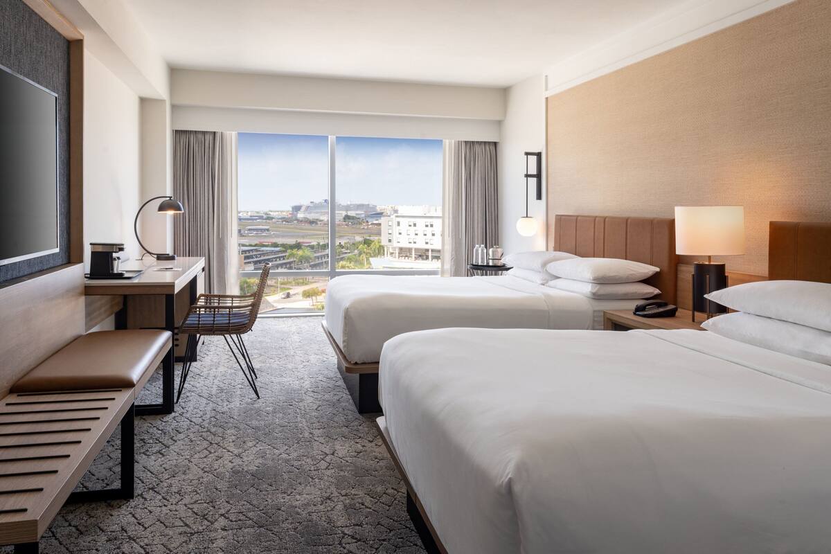 Une chambre d’hôtel avec deux lits, un bureau avec une chaise, une télévision et une vue sur la ville.