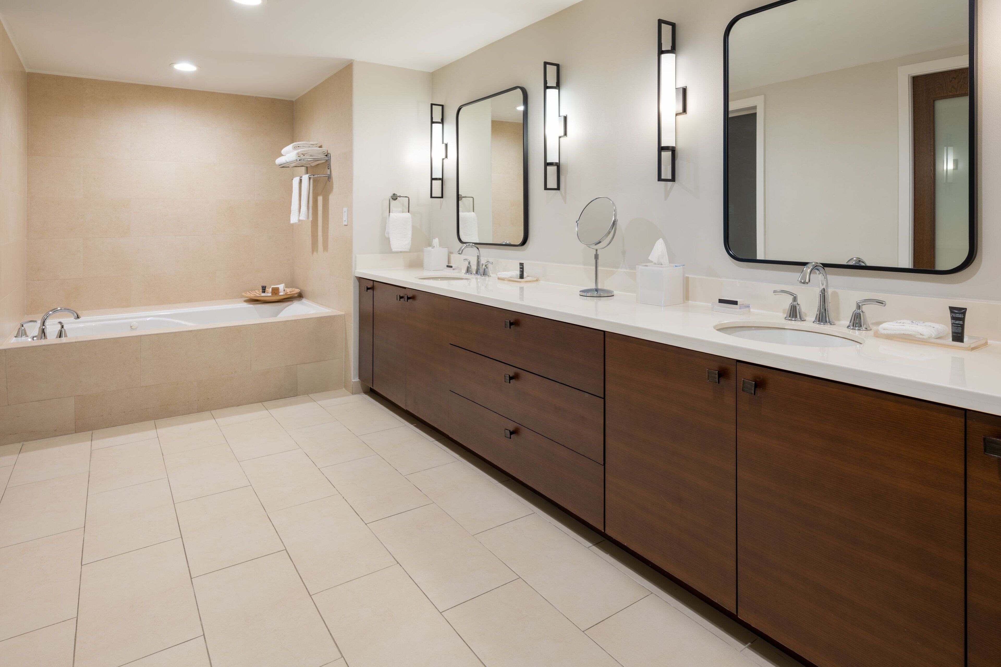 A modern bathroom with a bathtub, two sinks, a vanity with drawers, and a large mirror.