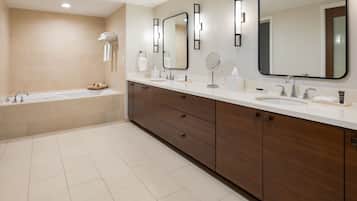 A modern bathroom with a bathtub, two sinks, a vanity with drawers, and a large mirror.