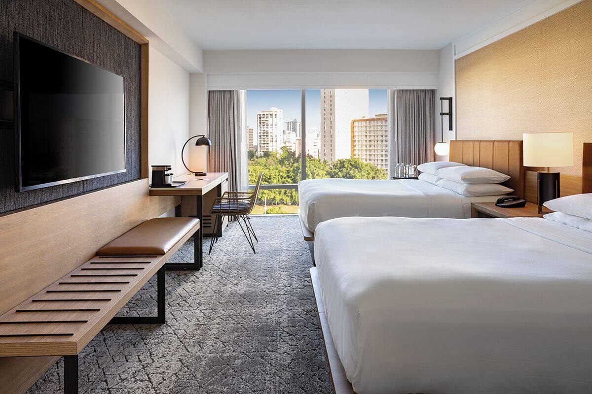 Une chambre d’hôtel avec deux lits, une télévision, un bureau avec une chaise et une vue sur la ville.