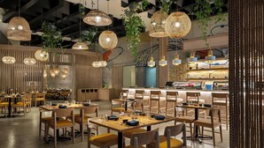 Un restaurant moderne avec des tables et des chaises en bois, des lustres en osier suspendus et un coin bar.