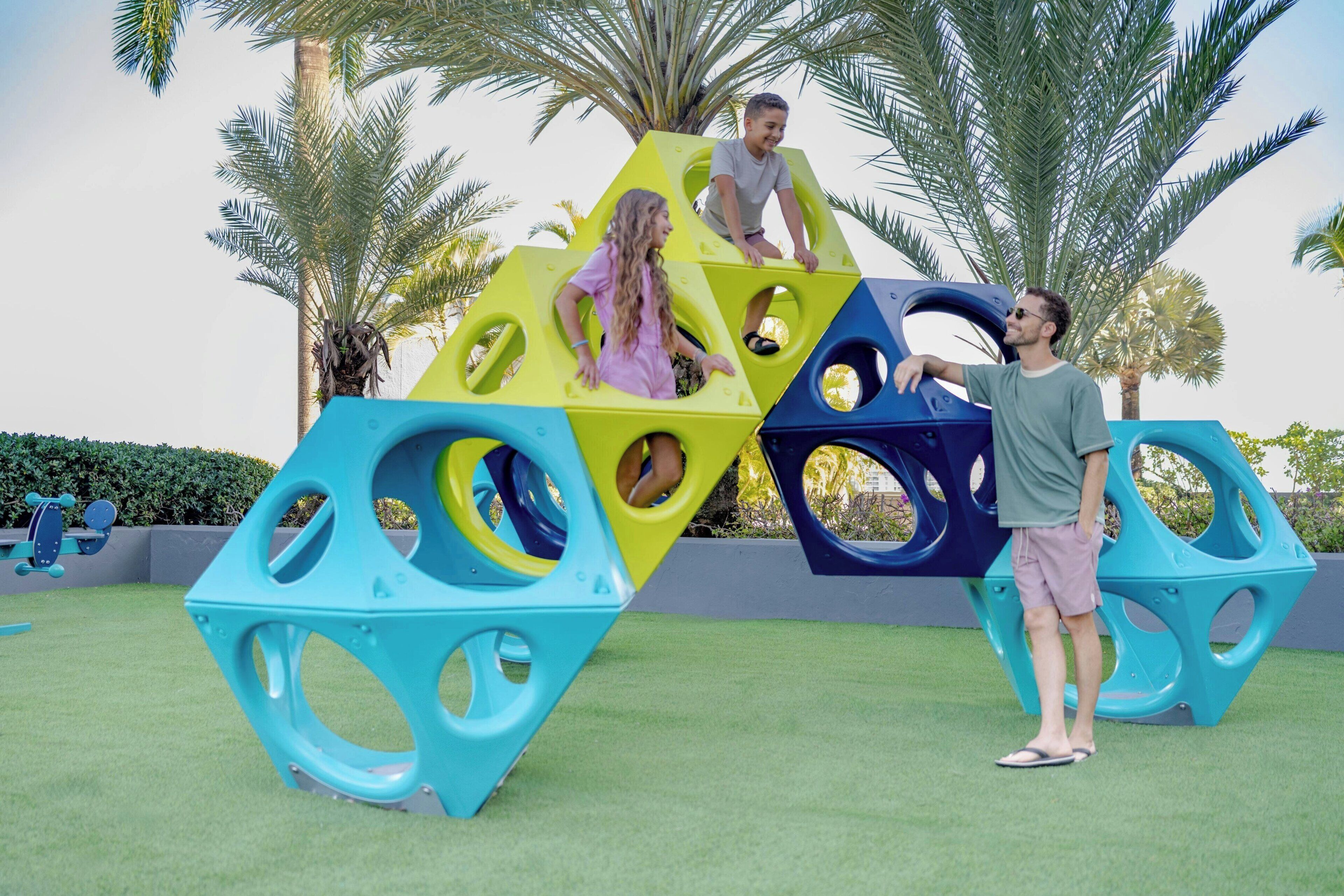 Une aire de jeux dotée de structures d’escalade aux formes géométriques et d’une surface recouverte de gazon synthétique.
