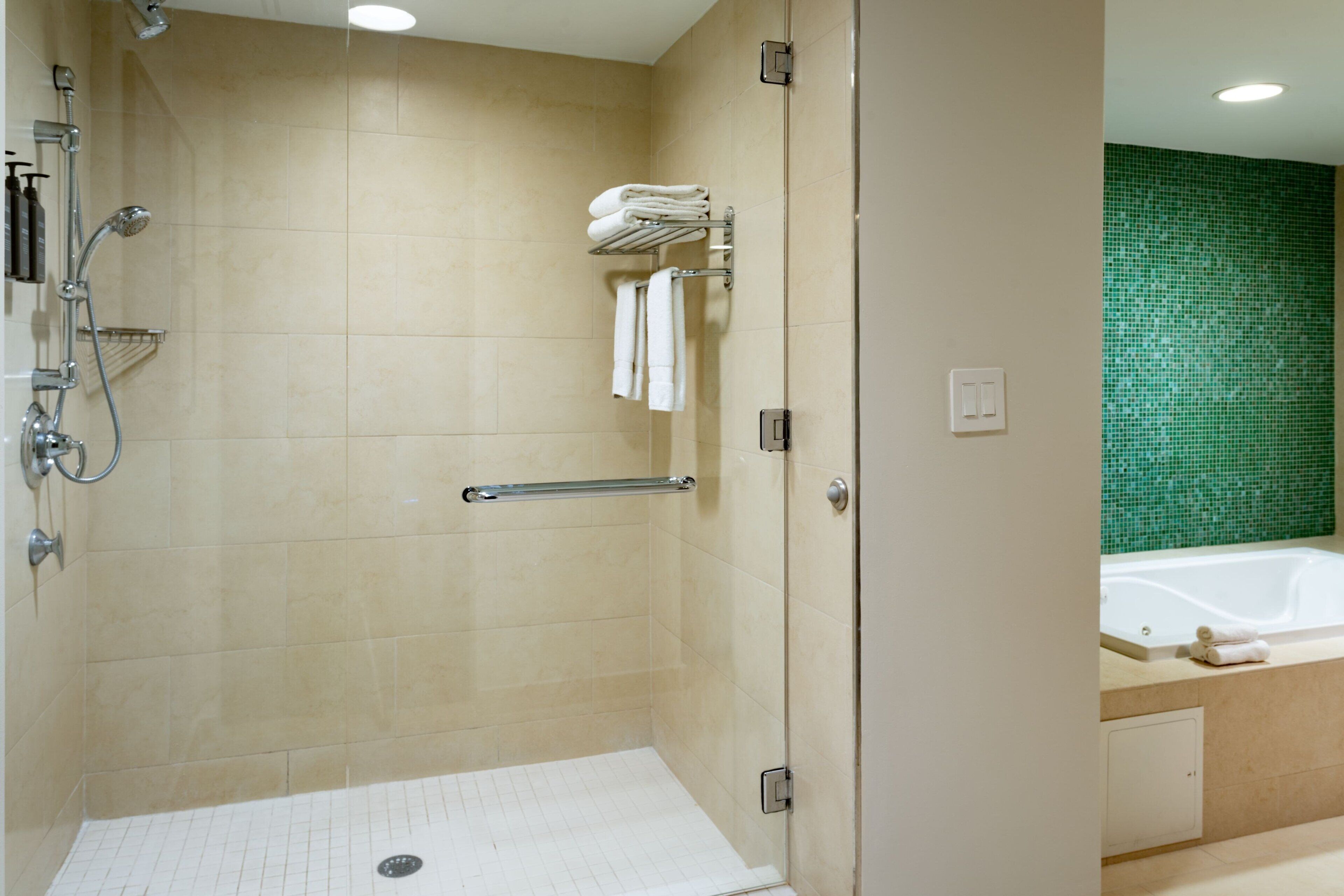 Un bagno moderno con doccia a filo pavimento, porta in vetro, parete rivestita in mosaico verde e vasca da bagno in vista.