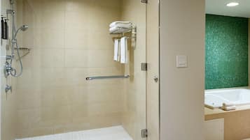 A modern bathroom with a walk-in shower, a glass door, a green mosaic wall, and a visible bathtub.