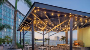 Une terrasse extérieure avec des tables et des chaises, des guirlandes lumineuses, un coin bar et une vue sur le paysage urbain.
