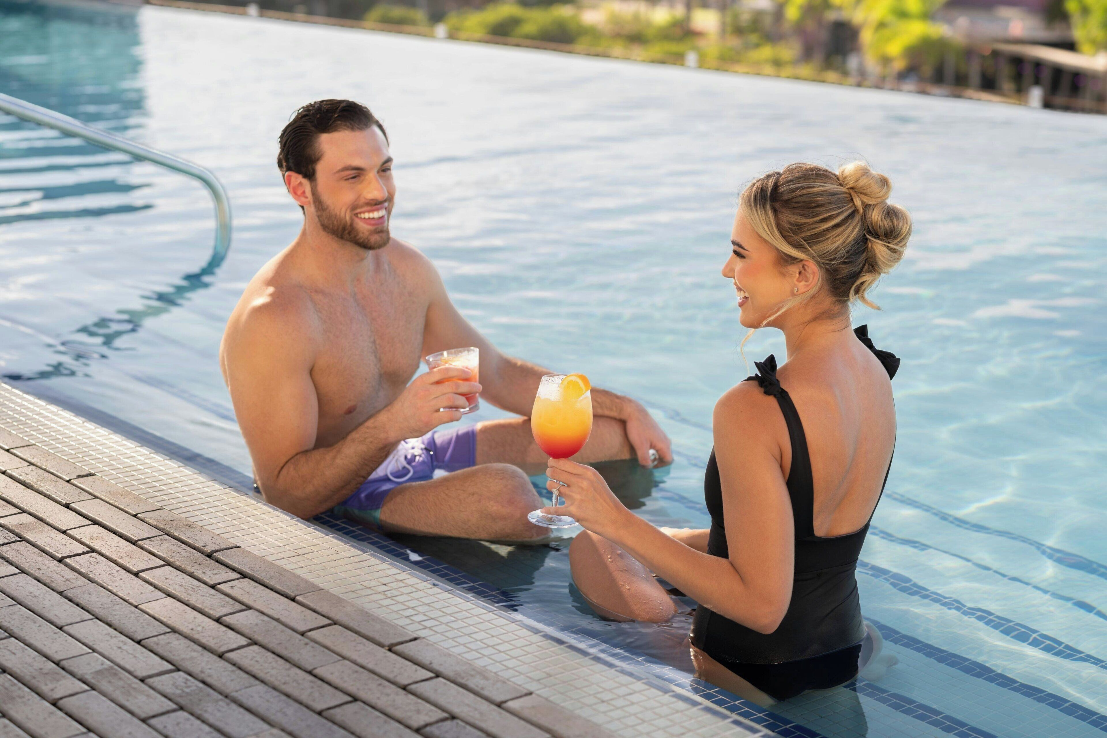 Una pareja en una piscina, cada uno con una bebida en la mano.