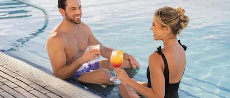 Una pareja en una piscina, cada uno con una bebida en la mano.