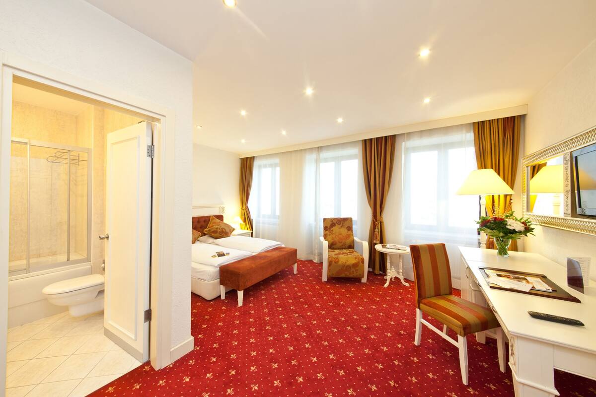 Une chambre d’hôtel comprenant un lit, un bureau, une chaise, une petite table, un espace douche et une salle de bain.