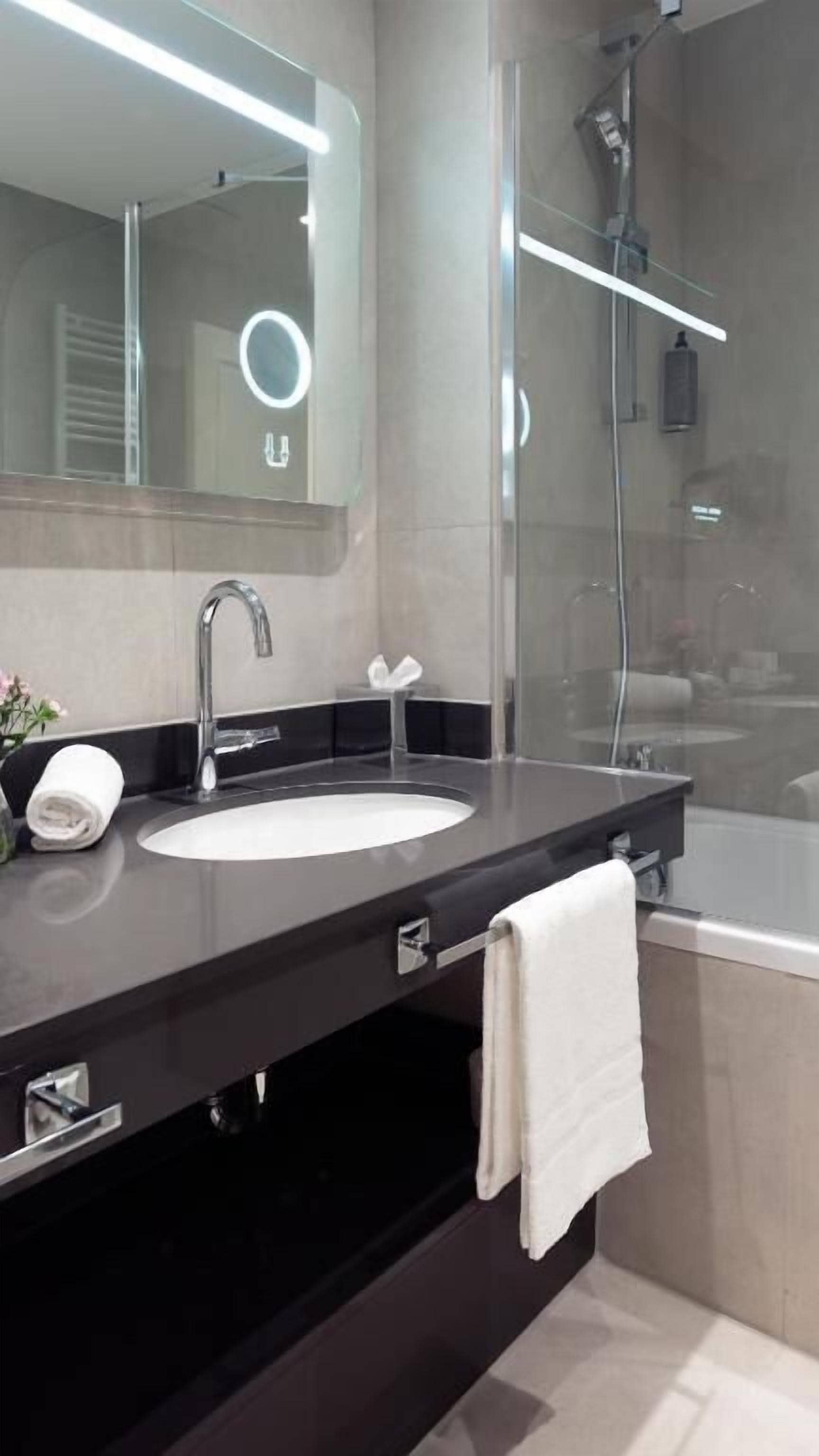 A modern bathroom with a large mirror, a white sink, a towel rack, and a shower area.