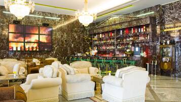 A luxurious lobby with marble walls, chandeliers, a bar area, and plush seating.