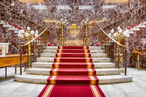 Eine prächtige Treppe mit Marmorwänden, Teppichstufen in Rot und aufwändig gestalteten Kronleuchtern.
