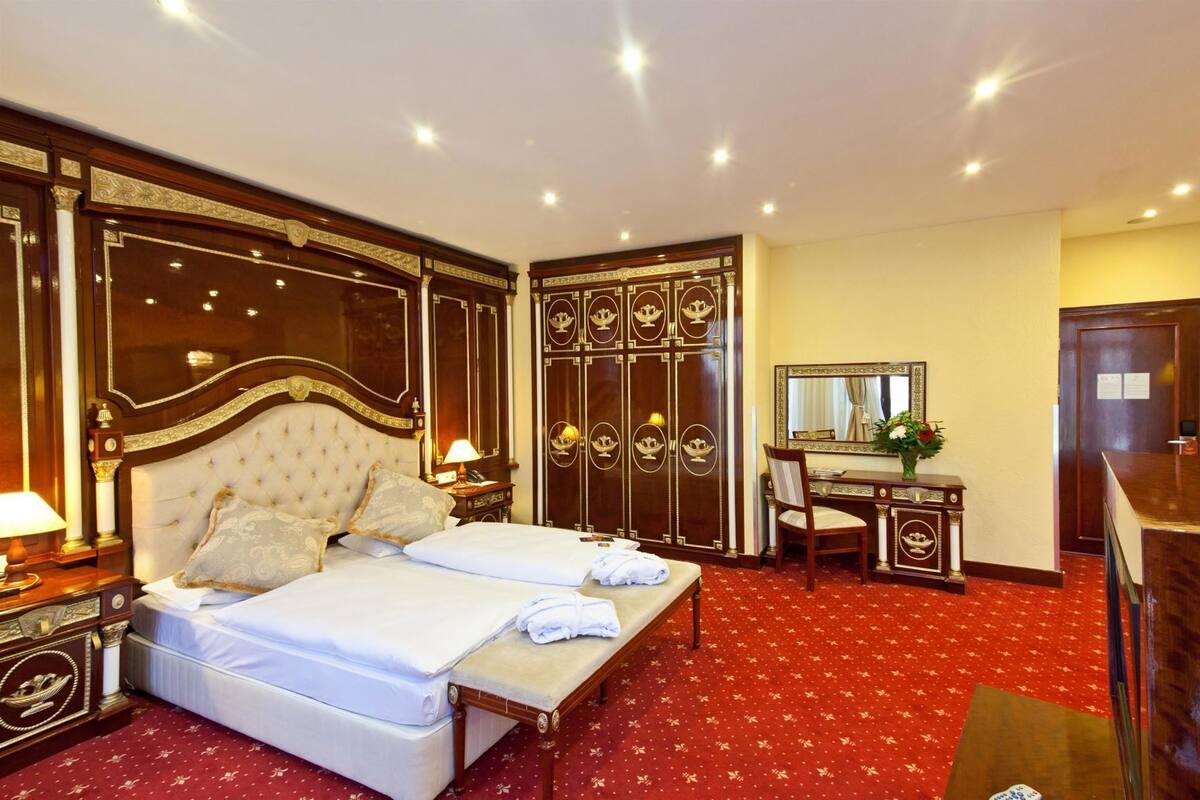 Une chambre d’hôtel avec un grand lit, un bureau avec une chaise, une armoire et un miroir.