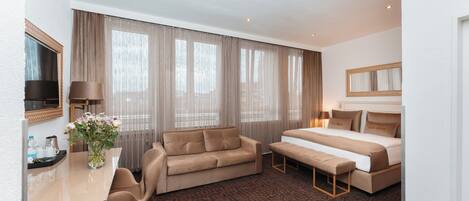 Quarto de hotel com cama, sofá, escrivaninha e uma cadeira.
