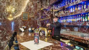 Um bar com bancada de mármore, um bartender e prateleiras cheias de garrafas de bebidas.