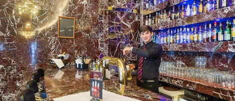 Un bar con mostrador de mármol, un barman y estanterías llenas de botellas de licor.
