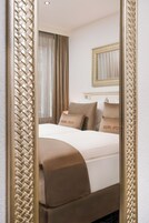 Quarto de hotel com cama, cortinas, espelho e painel decorativo na parede.
