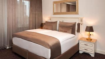 Habitación de hotel con una cama grande, una mesita de noche con lámpara, un espejo sobre la cama y una ventana con cortinas.