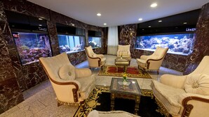 Une chambre luxueuse aux murs de marbre, dotée d’un grand aquarium et de fauteuils confortables.