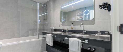 A modern bathroom with a glass shower enclosure, dual sinks, and a large mirror with integrated lighting.