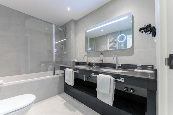 Un baño moderno con cabina de ducha de vidrio, lavamanos dobles y un espejo grande con iluminación integrada.