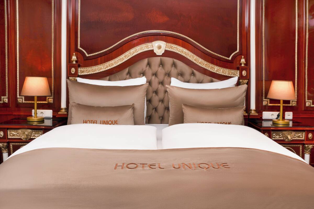 Une chambre d’hôtel avec un grand lit, deux tables de chevet avec des lampes et une tête de lit au motif capitonné.