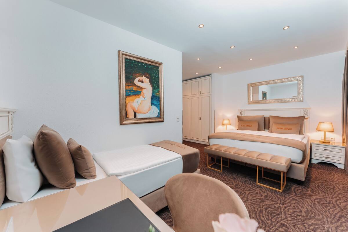 Une chambre d’hôtel comprenant un lit, un bureau, une chaise, un banc, un tableau, une armoire et un miroir.