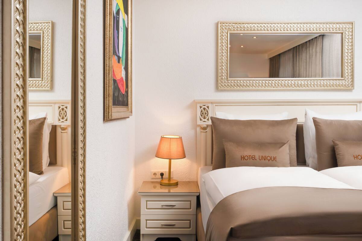 Une chambre d’hôtel avec un lit, des tables de chevet, une lampe, un miroir et un tableau au mur.