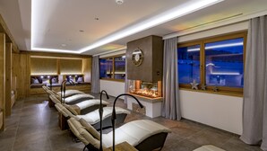 A spa room with multiple massage chairs, a fireplace, and a view of a snowy landscape through large windows. - Naturhotel Kitzspitz (Sankt Jakob in Haus)