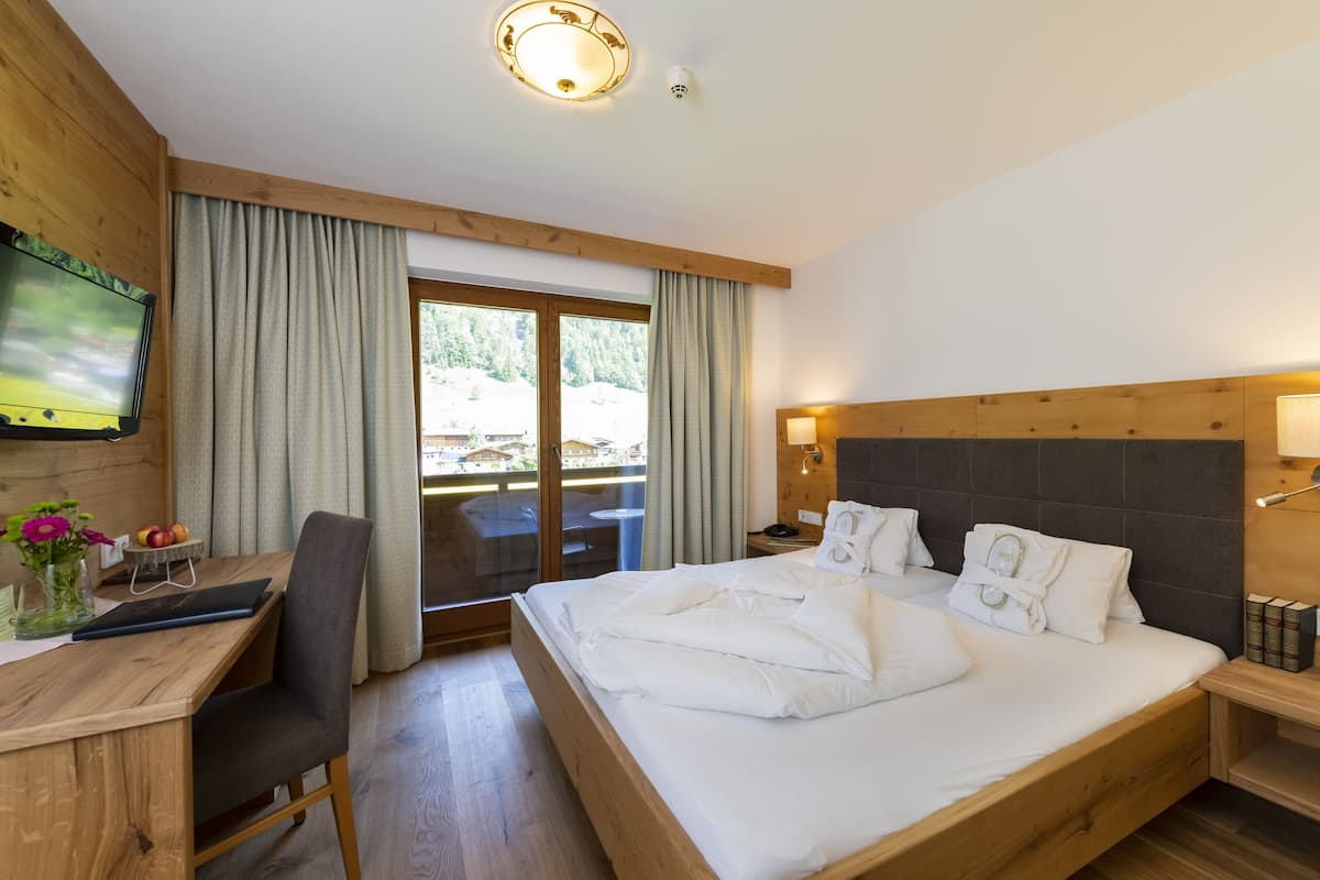 A hotel room with a wooden bed, a desk with a chair, a TV, and a view of the outdoors.