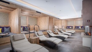 A spa area with multiple sun loungers, wooden walls, and a stone floor. - Naturhotel Kitzspitz (Sankt Jakob in Haus)