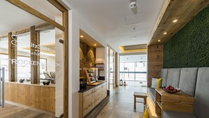 A modern interior with a wooden reception desk, a seating area with a grey sofa, and a green wall. - Naturhotel Kitzspitz (Sankt Jakob in Haus)