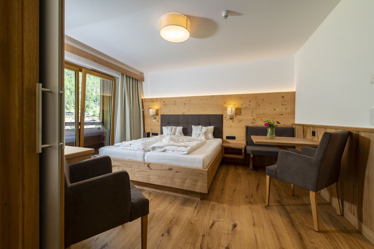 A modern hotel room with a wooden bed, a dining table, and a view of the outdoors.