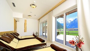 A spa room with massage tables, a large window with a mountain view, and a vase with flowers. - Naturhotel Kitzspitz (Sankt Jakob in Haus)