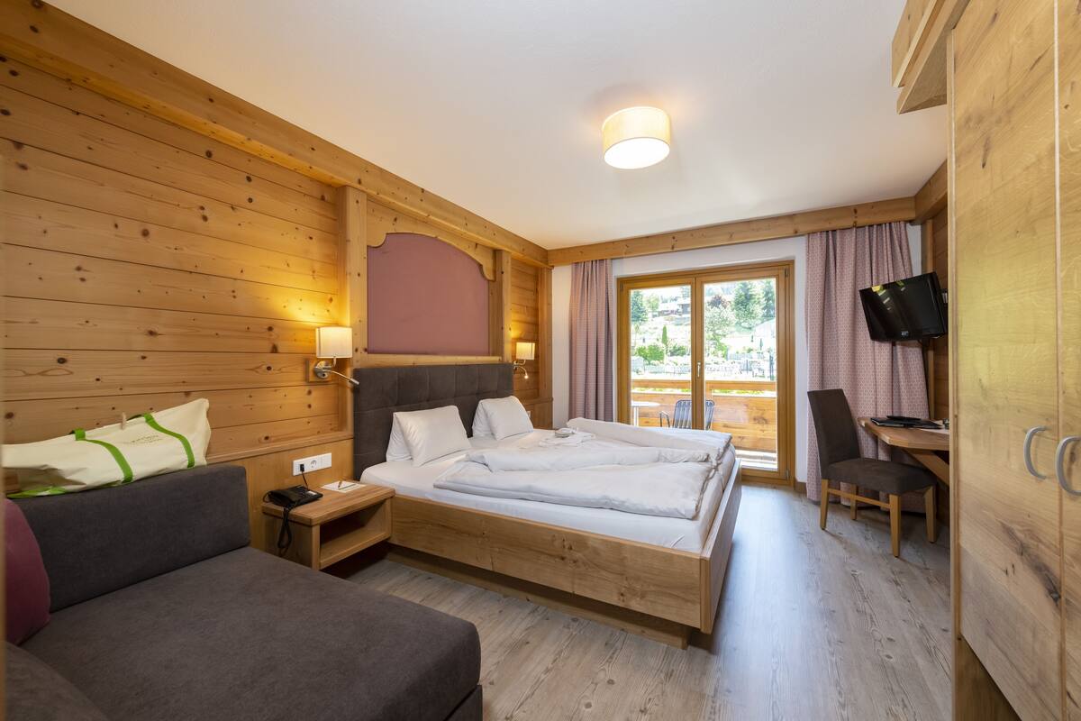 A wooden-paneled room with a bed, a sofa, a desk, and a TV.