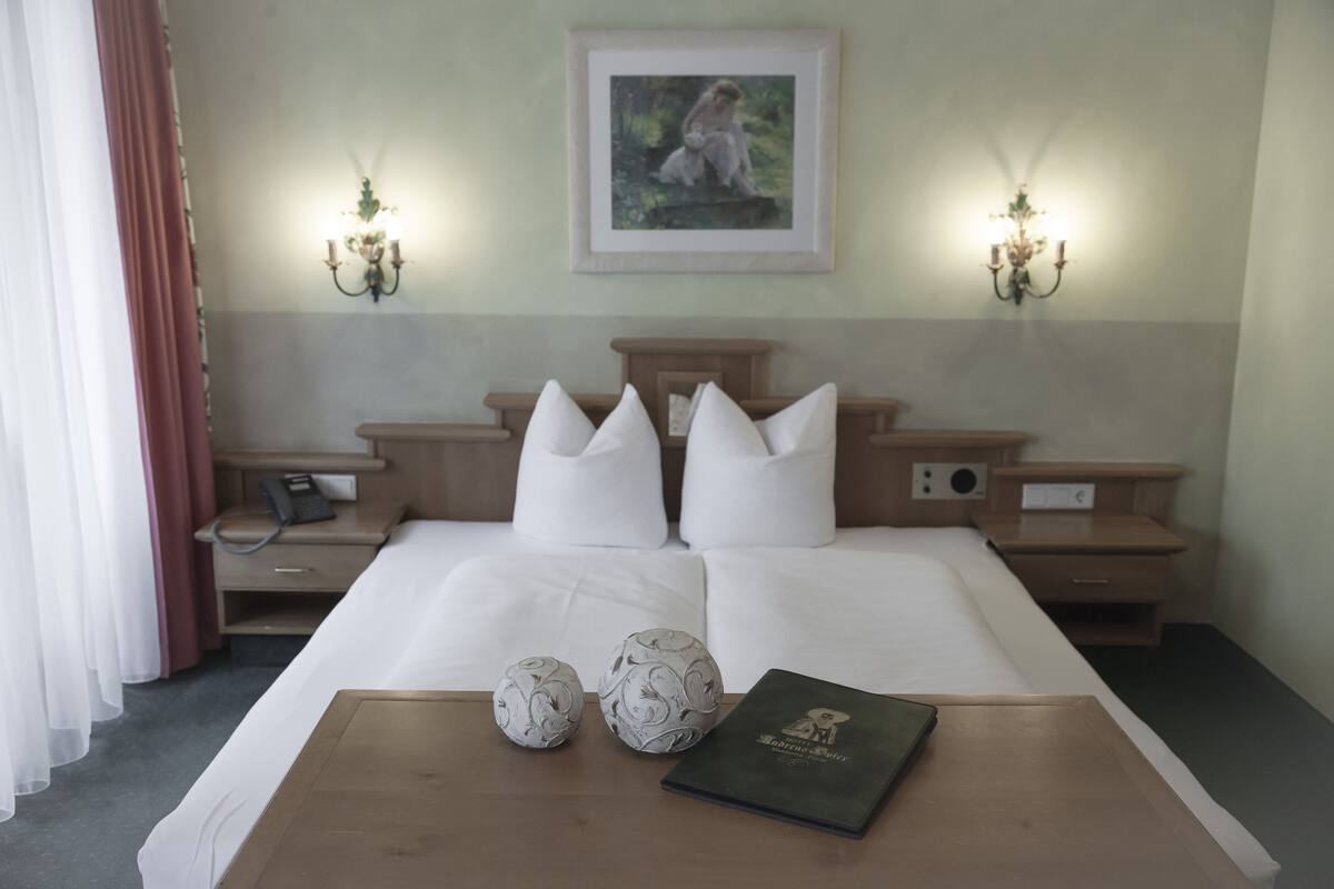 A neatly made bed with white linens, two wall-mounted lamps, a framed picture above the bed, and a bedside table with a phone and a book.