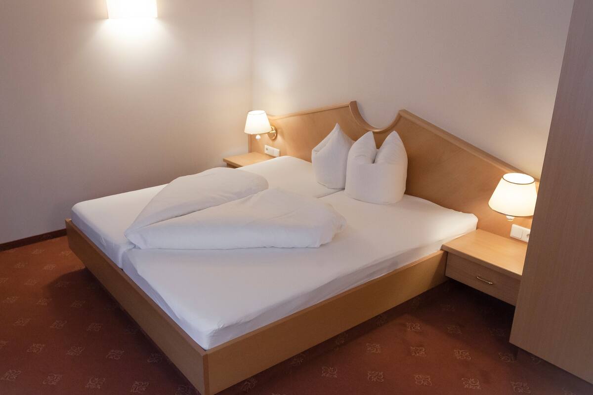 A neatly made bed with white linens, two bedside lamps, and a wooden headboard.