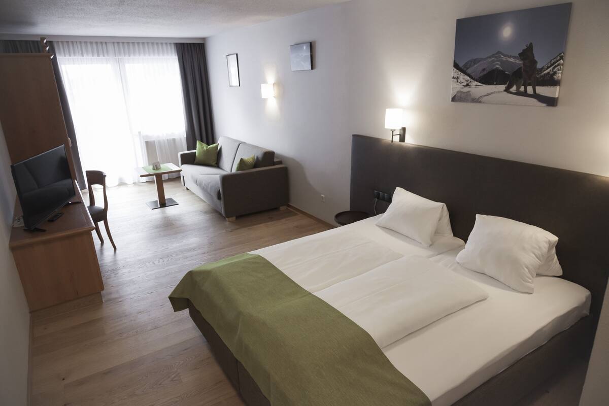 A hotel room with a large bed, a sofa, a desk with a TV, and a painting on the wall.
