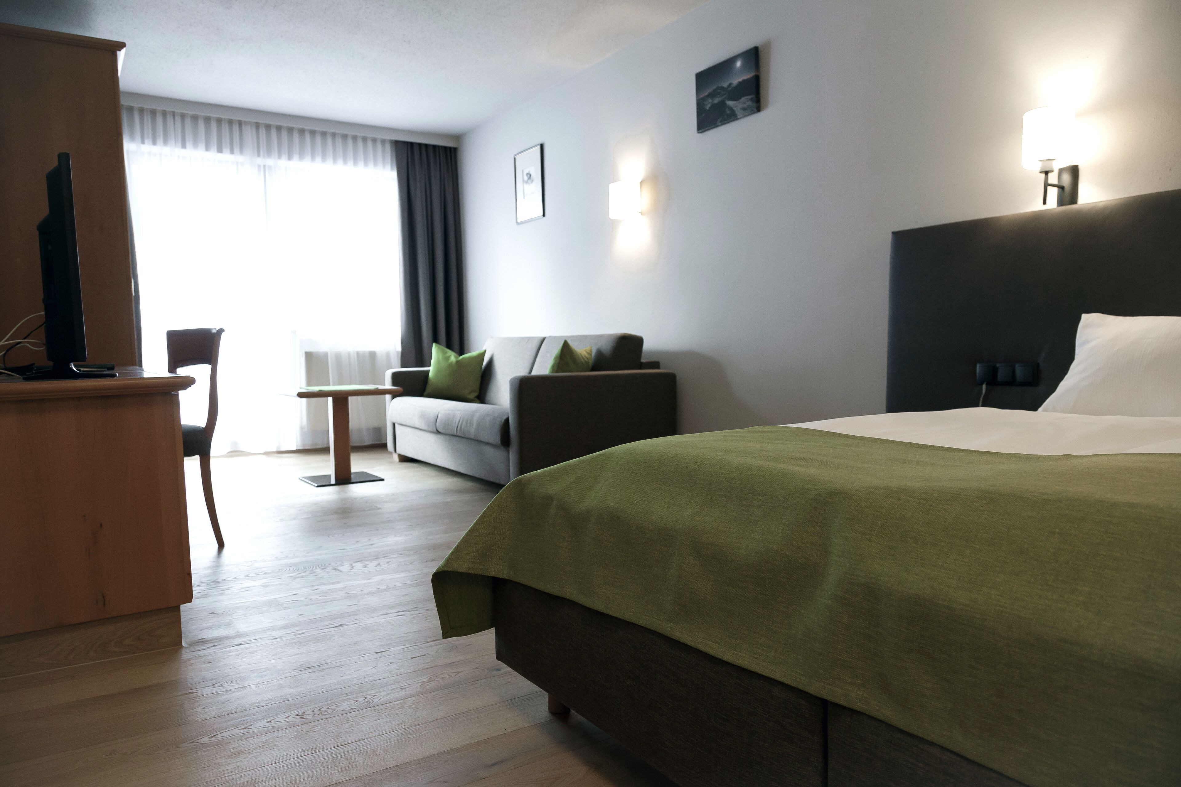 Ett hotellrum med en säng, ett skrivbord, en stol, en soffa och utsikt över omgivningarna.