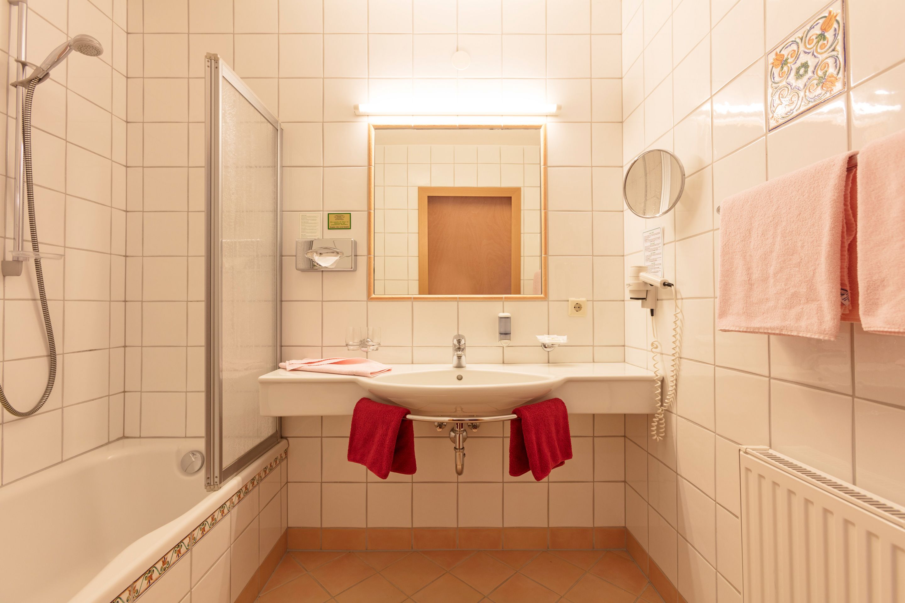 A bathroom with a shower, sink, mirror, and towels.