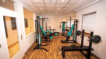 A gym with exercise equipment, wooden flooring, and a window with blinds.