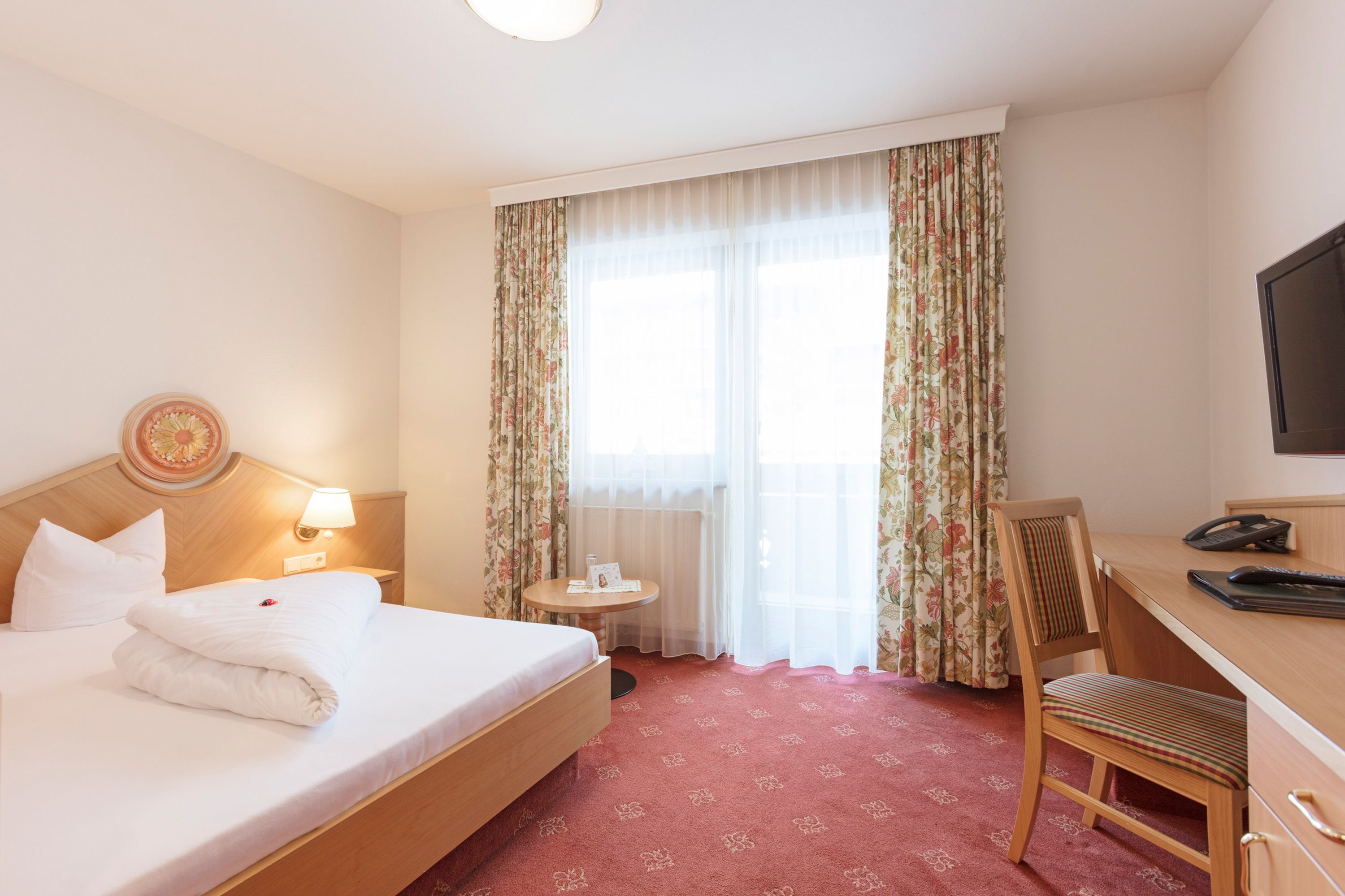 Ein Hotelzimmer mit Bett, Schreibtisch, Stuhl, kleinem Tisch und Fernseher.