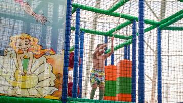 Zona infantil con cerramiento de red, estructuras de juego coloridas y un mural de una sirena.