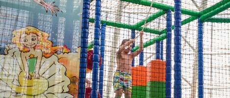 A children's play area with a net enclosure, colorful play structures, and a mural of a mermaid.