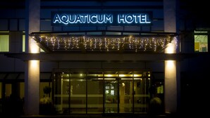 The exterior of the Aquaticum Hotel with a prominent illuminated sign, a glass entrance, and string lights above the entrance. - Aquaticum Debrecen Thermal and Wellness Hotel (Debrecen)